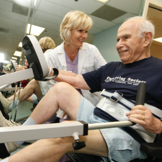 Older man exercising with a nurse standing beside him