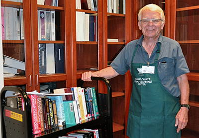 Old man standing beside a pile of books