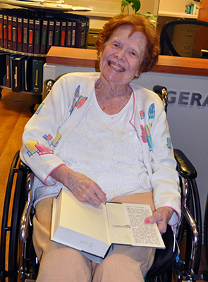 an old lady smiling while seating on a wheel chair while holding a book