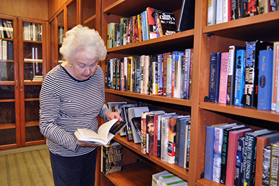 An old lady standing in front of a bookshelf while reading a book