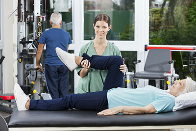 Elderly women getting a leg therapy with a nurse and an old man behind them