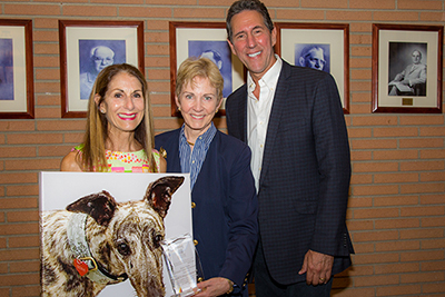 Three people holding a plaque and a portrait of a dog